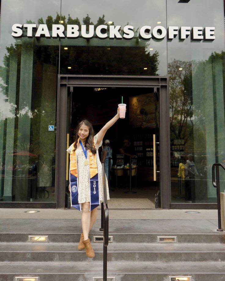 a woman standing on the steps holding up a coffee cup in front of a starbucks