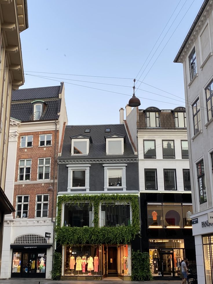 a row of buildings with people walking on the sidewalk in front of them and one building that has ivy growing all over it