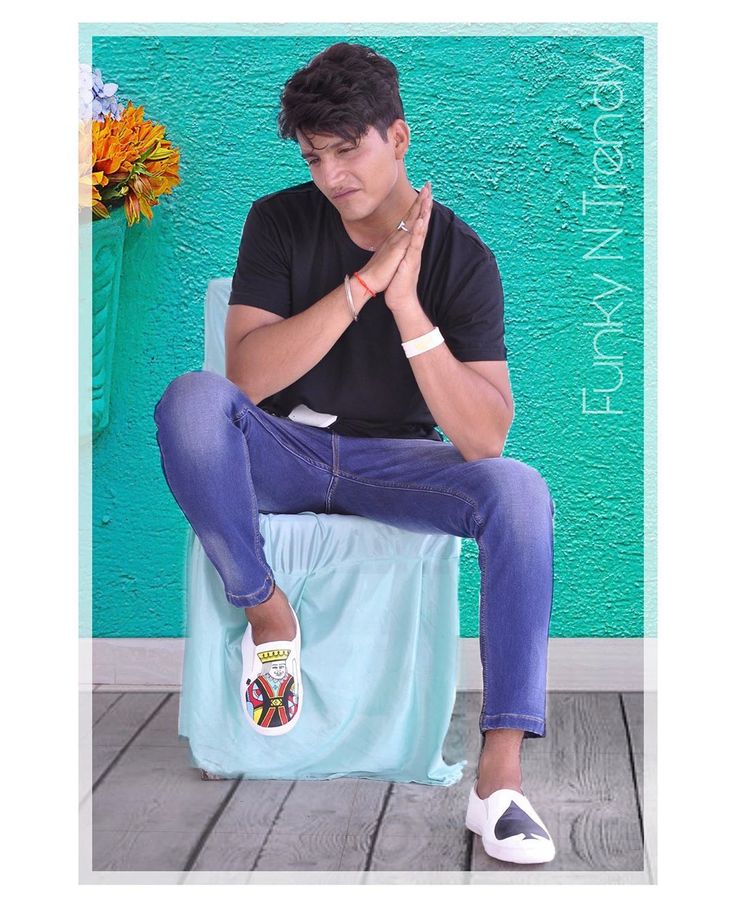 a man sitting on top of a blue chair next to a flower pot and wearing white shoes