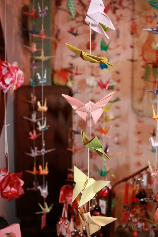 a bunch of origami birds hanging from strings in a room filled with other decorations