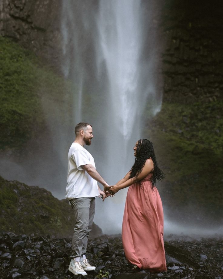 a man and woman holding hands in front of a waterfall