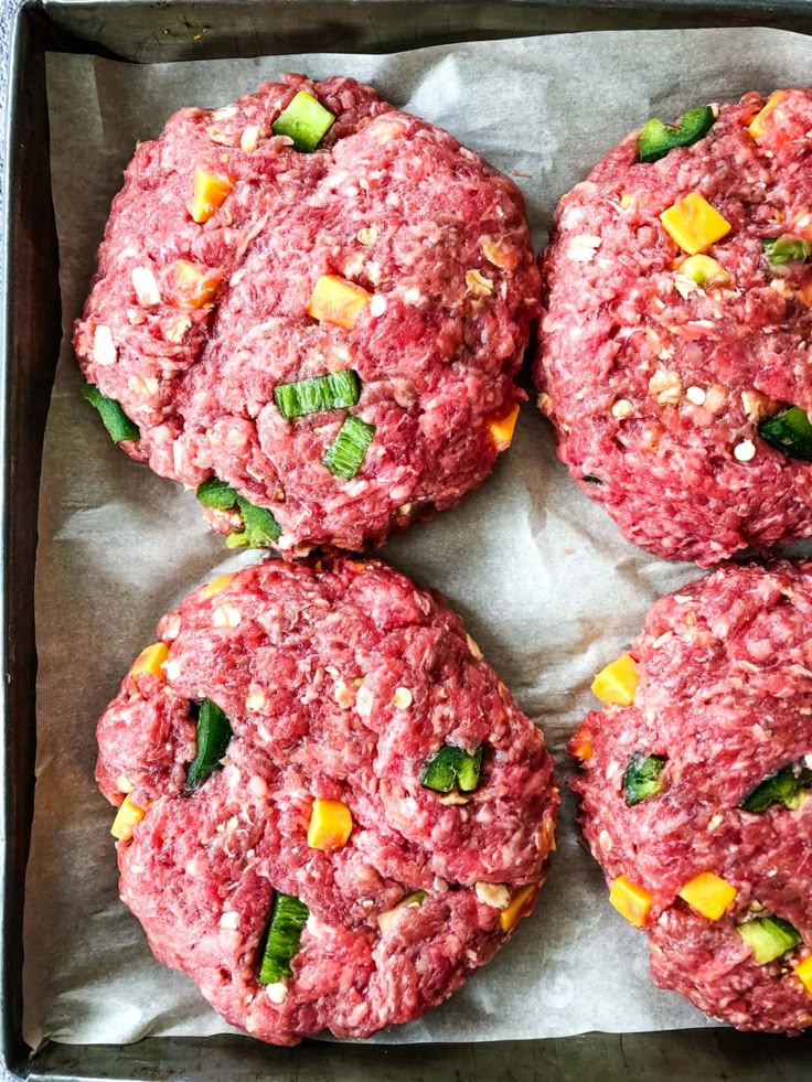 four hamburger patties in a metal pan on top of wax paper with toppings