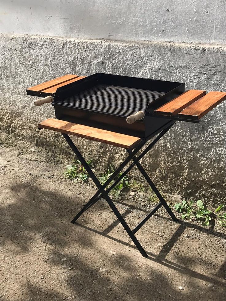 a grill sitting on top of a wooden table next to a cement wall and grass