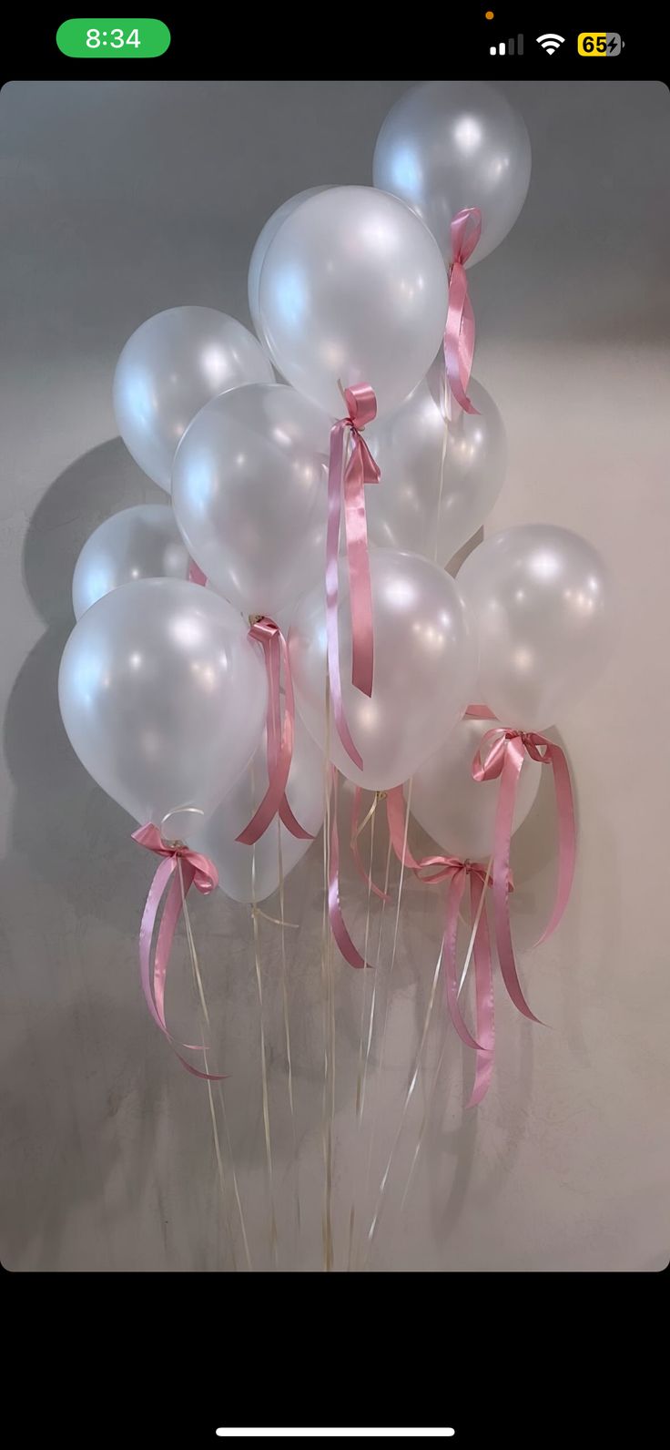 a bunch of white balloons with pink ribbons