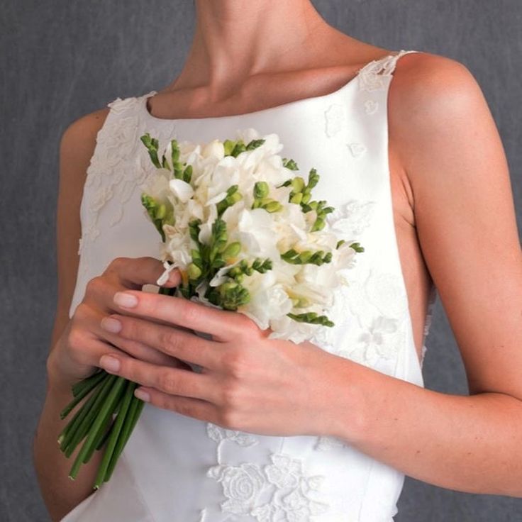 a woman in a wedding dress holding a bouquet of white flowers with green leaves on it