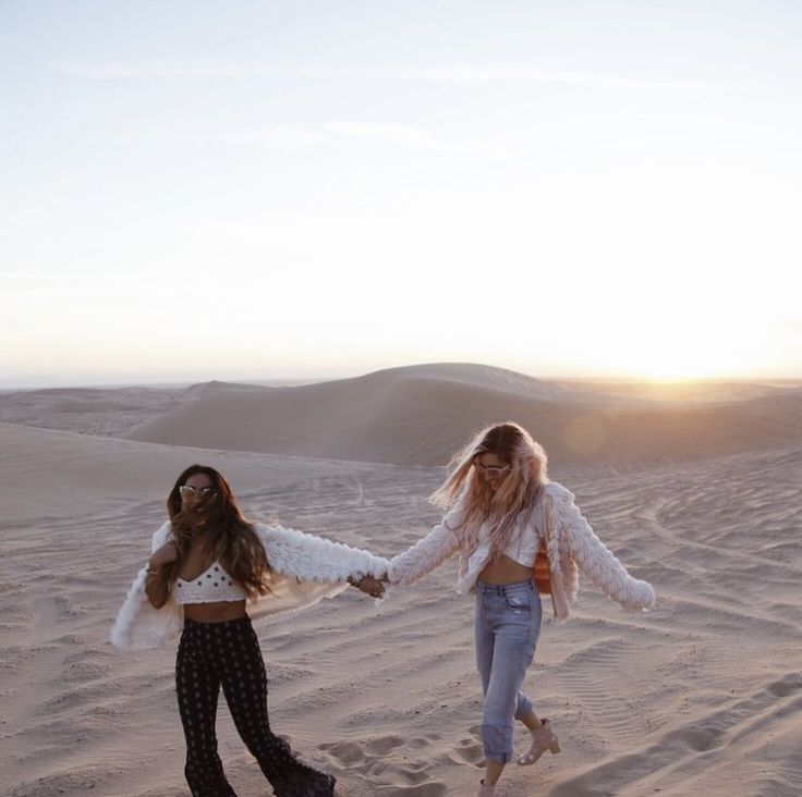 two girls walking in the sand holding hands