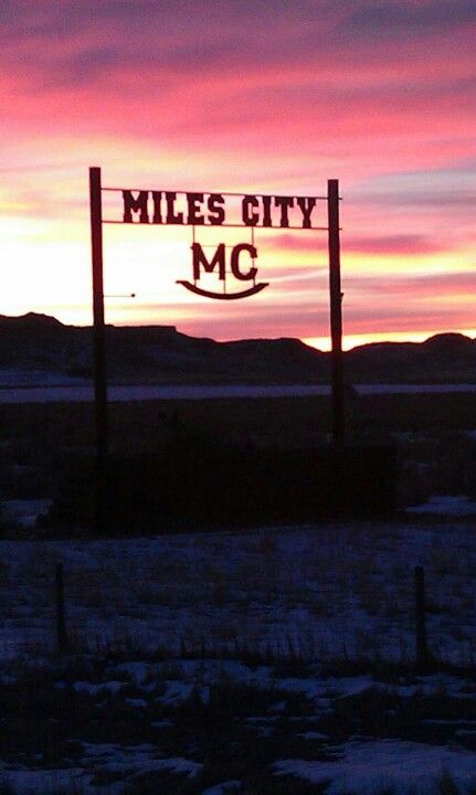 a sign that reads miles city mc in front of a sunset with mountains behind it