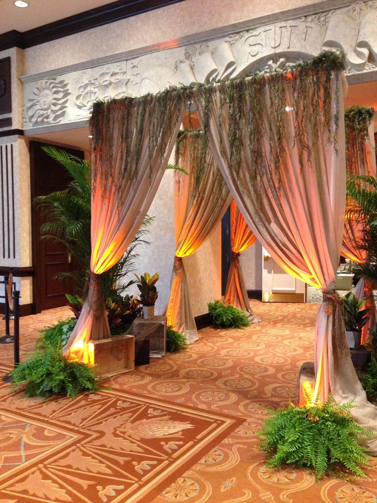 an indoor area with curtains and plants on the floor, lit up by candle lights