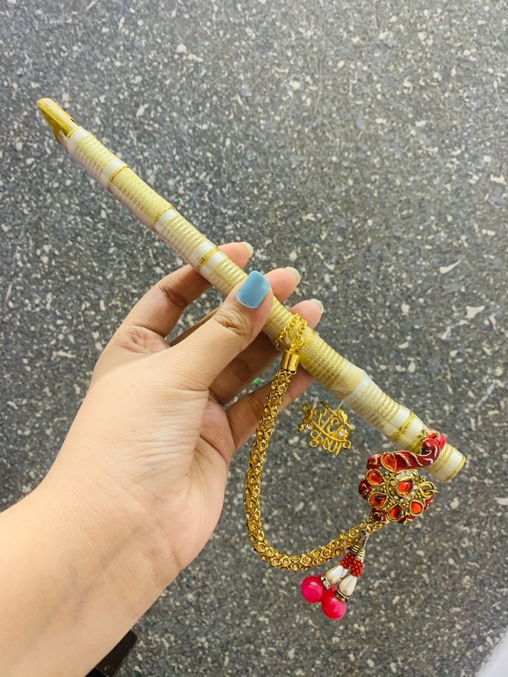 a hand holding a gold and red colored pen with beads on it's end