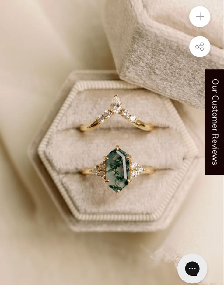 two gold rings with green and white stones on them, sitting in a velvet box