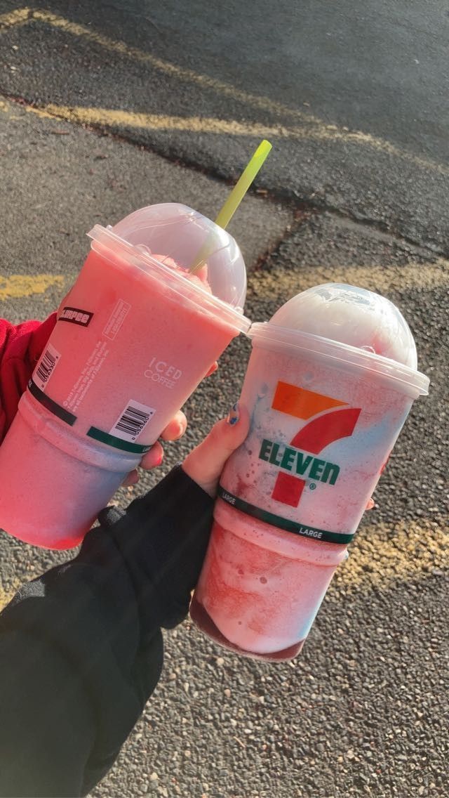 two pink drinks are being held by someone's hand on the side of the road