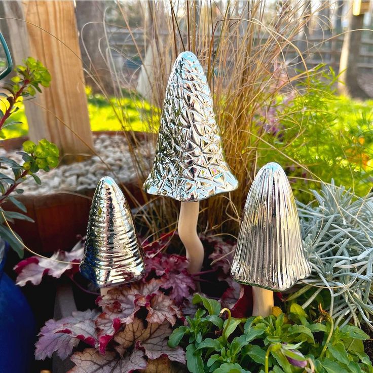 three small metal mushrooms sitting in the middle of some potted plants and other plants