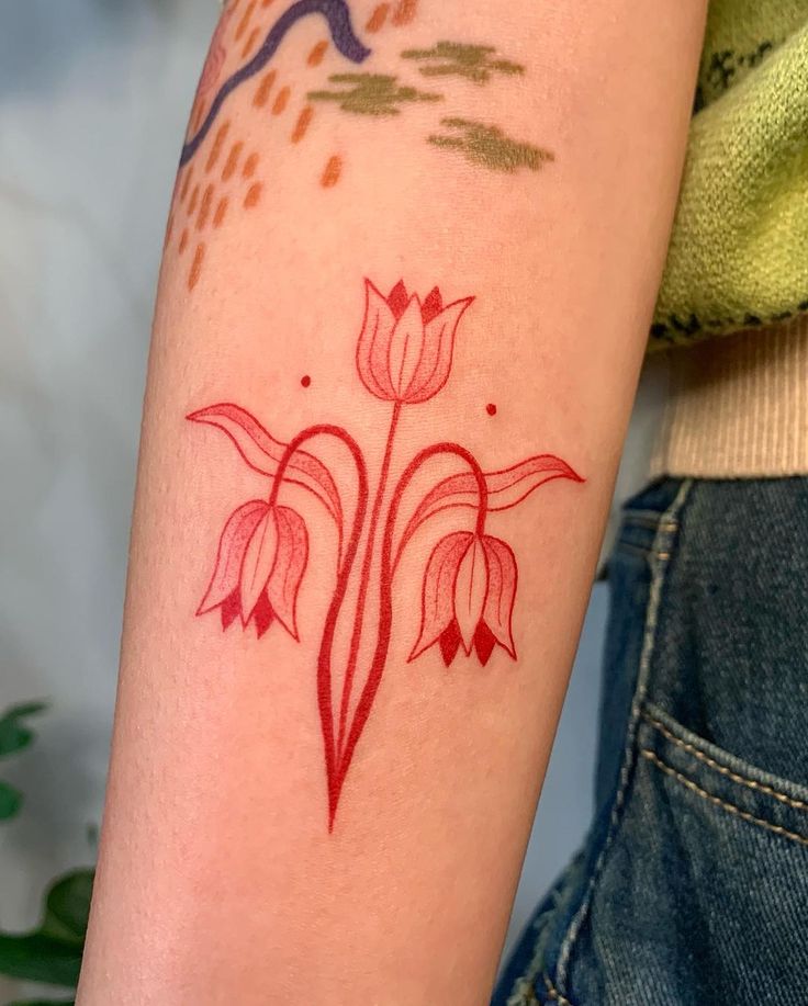 a woman with a tattoo on her arm has a red flower design on it's left arm