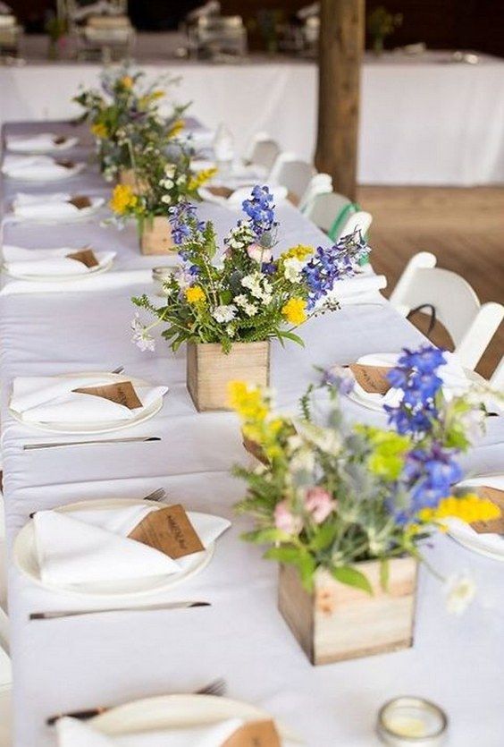 a long table is set with white linens and flower centerpieces for the tables