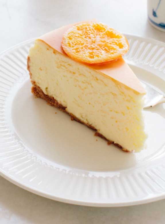 a slice of cheesecake on a white plate with an orange garnish in the middle