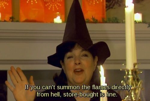 a woman wearing a witches hat standing in front of a candle with her hands up