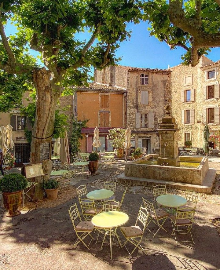 an outdoor courtyard with tables and chairs in the shade, surrounded by stone buildings on either side