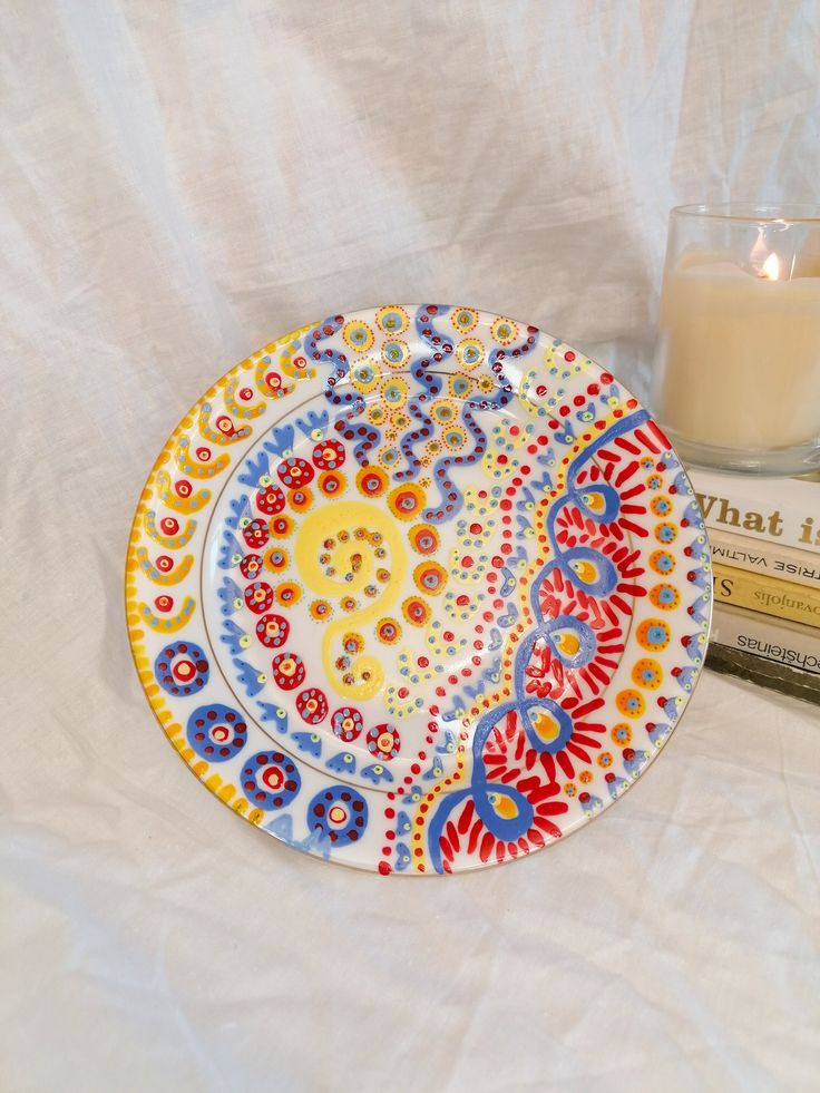 a colorful plate sitting on top of a table next to a candle and some books