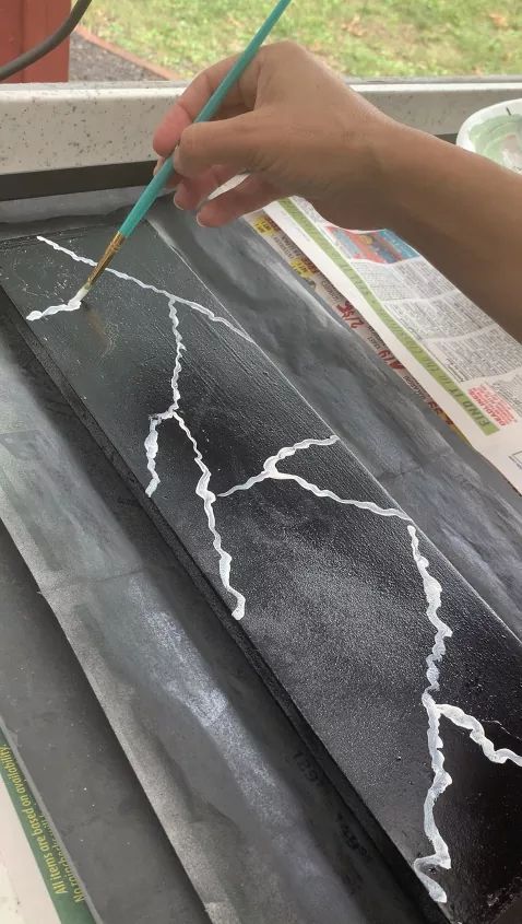 someone is drawing lightning on a piece of black paper with a green pencil in their hand