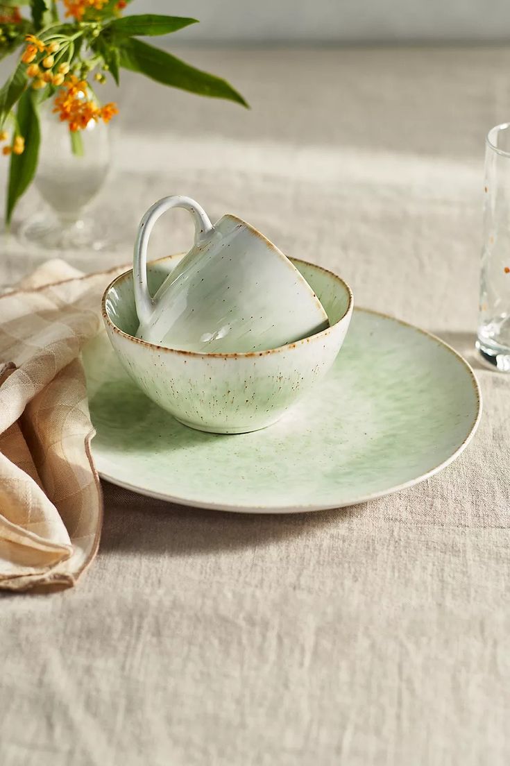 there is a cup and saucer on the table next to a vase with flowers in it