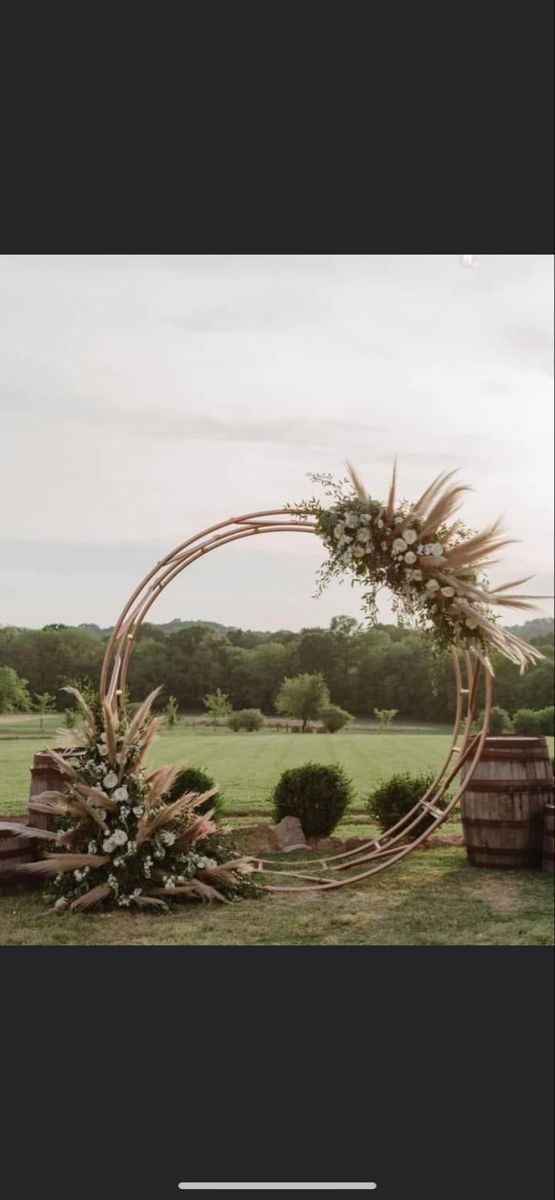 a wedding arch with flowers and greenery on the grass in front of an open field