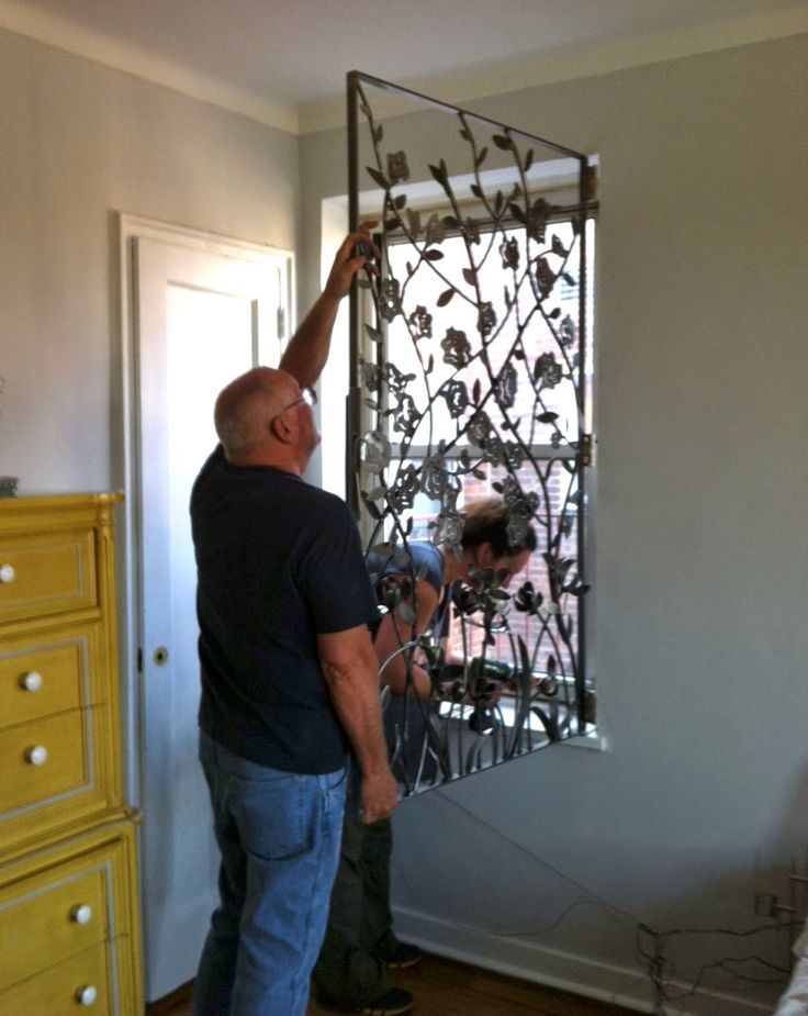 two men working on a metal screen in a room with yellow drawers and white walls