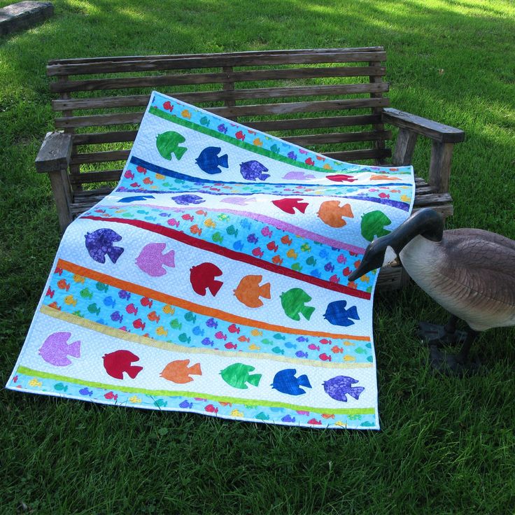 a duck sitting on top of a grass covered field next to a quilted blanket