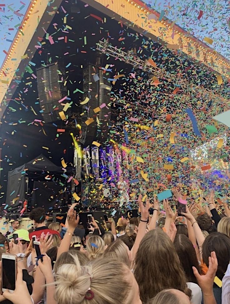 a crowd of people holding up cell phones in front of a stage with confetti