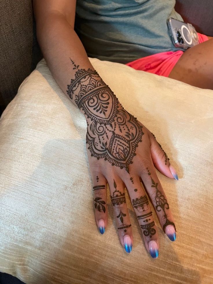 a woman's hand with henna tattoos on her left and right palm, resting on a pillow