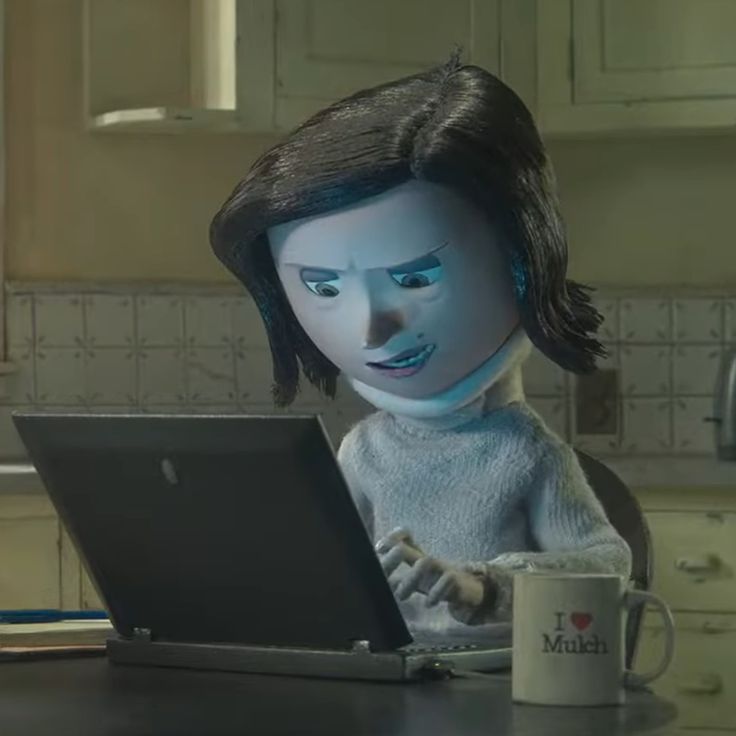 a woman sitting in front of a laptop computer on top of a kitchen counter next to a cup