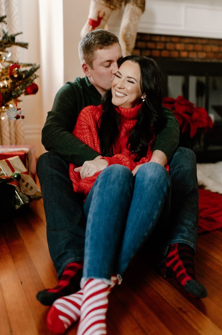 a man and woman sitting on the floor in front of a christmas tree