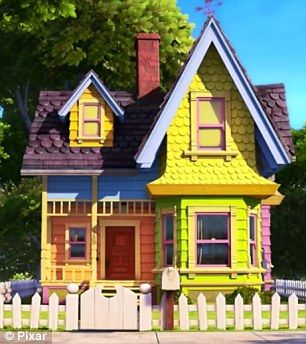 a yellow and blue house sitting on the side of a road next to a white picket fence