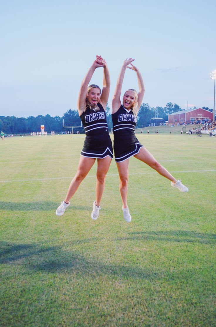 two cheerleaders in black and white outfits are doing a handstand on the field