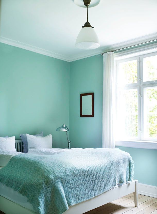 a bed sitting under a window next to a lamp on top of a hard wood floor