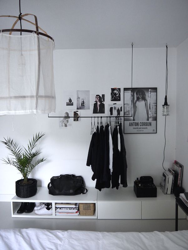 a white room with clothes hanging on the wall, and a bed in the foreground