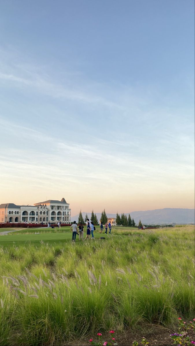 people are walking through the grass in front of a large building