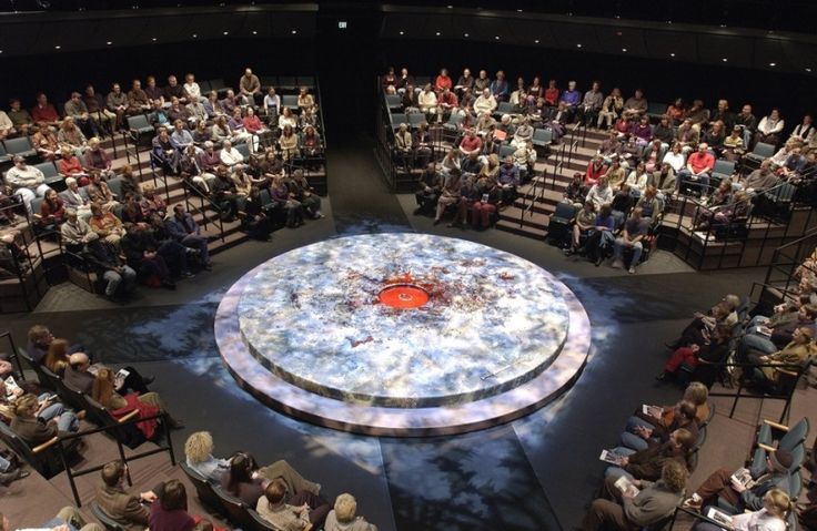 a large group of people sitting in front of a stage with a red object on it