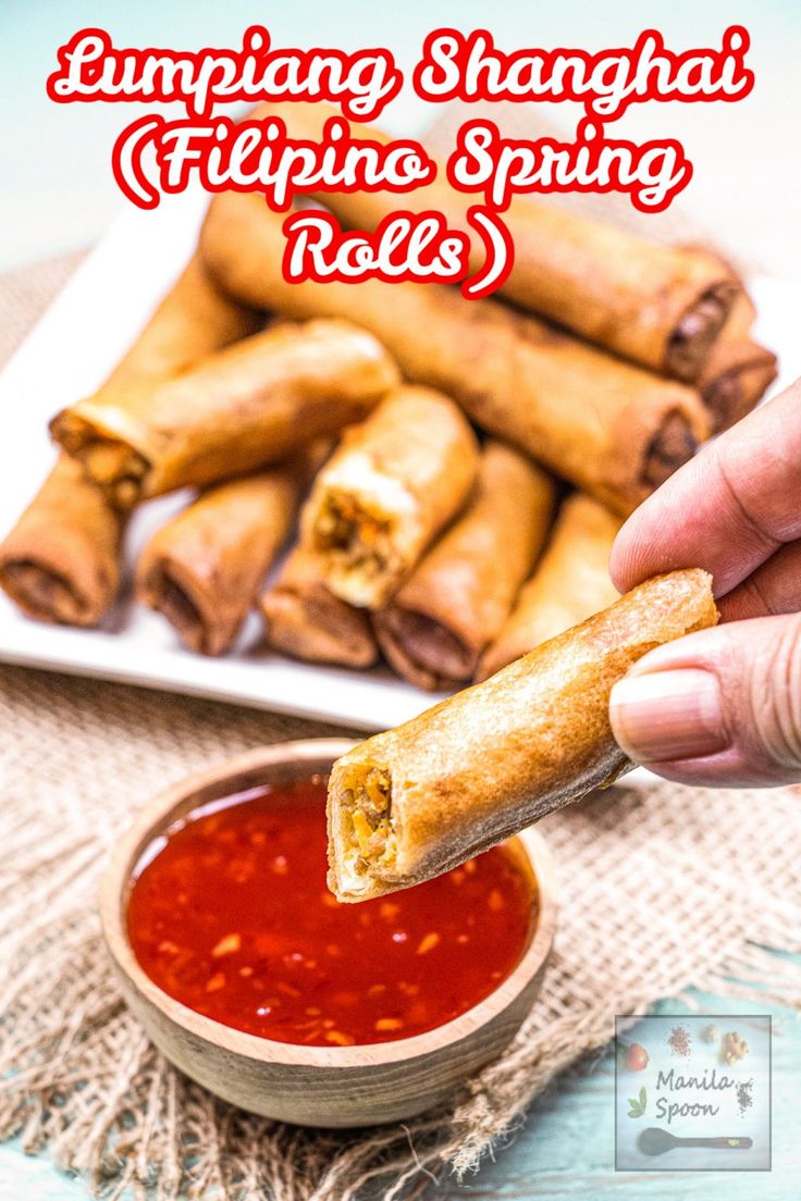 someone is dipping some food in a small bowl with sauce on the side and another plate full of spring rolls