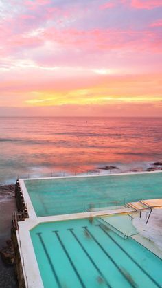 an empty swimming pool in front of the ocean at sunset with pink and blue sky