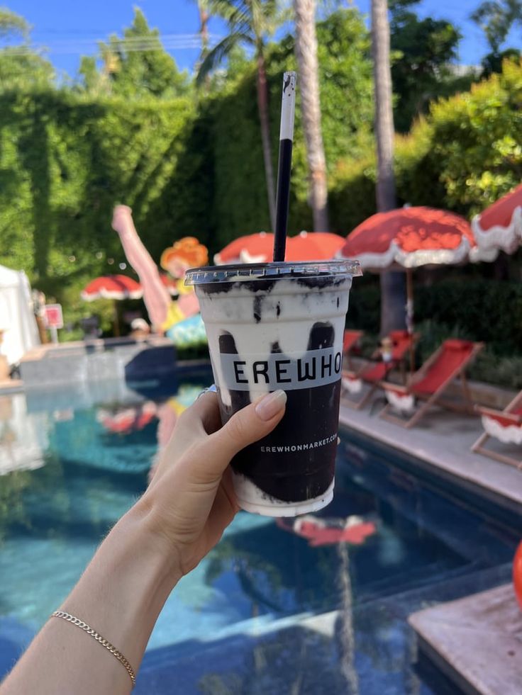 a person holding up an ice cream sundae next to a pool with umbrellas