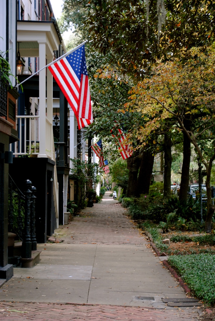 an american flag is flying in the wind on a sidewalk next to some buildings and trees