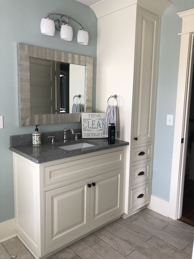 a white bathroom with blue walls and gray counter tops, along with two mirrors on the wall