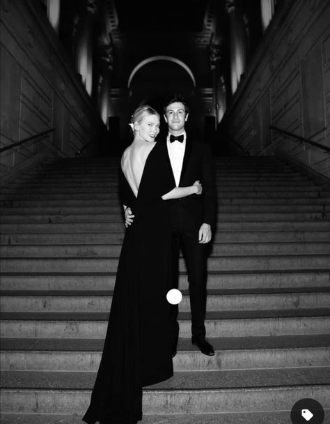 a man and woman standing on the steps in front of some stairs wearing tuxedos