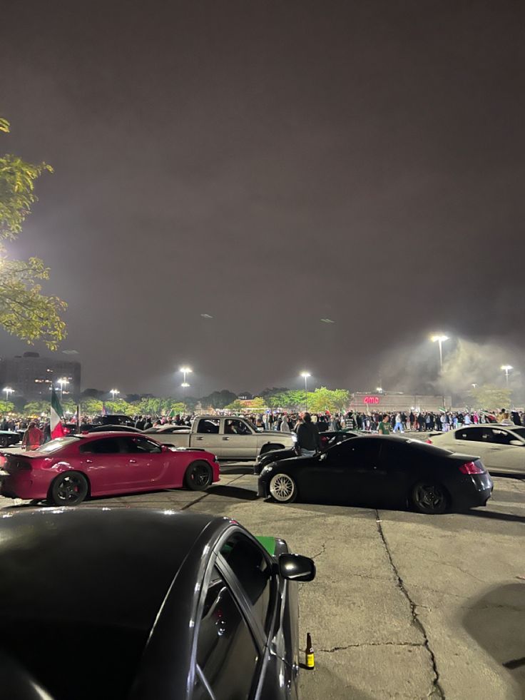 several cars parked in a parking lot with people standing around the area at night time