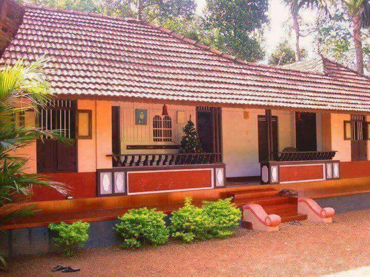 a small white house with red trim and brown shutters on the front, surrounded by greenery