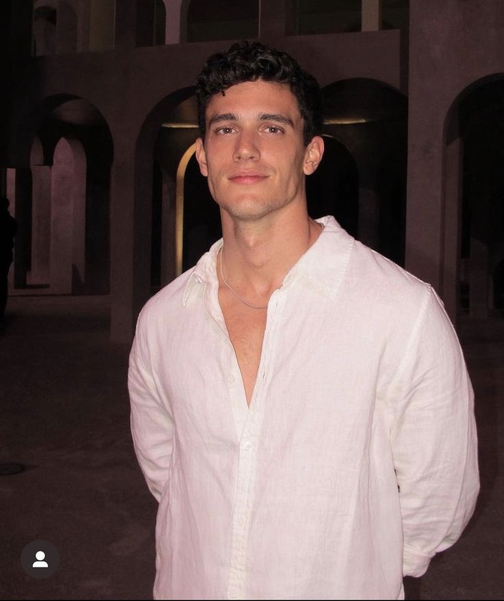 a man in a white shirt is posing for the camera with his hands in his pockets