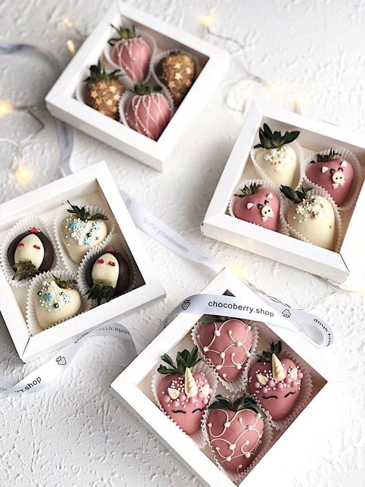 four boxes filled with chocolate covered strawberries on top of a white tablecloth next to string lights