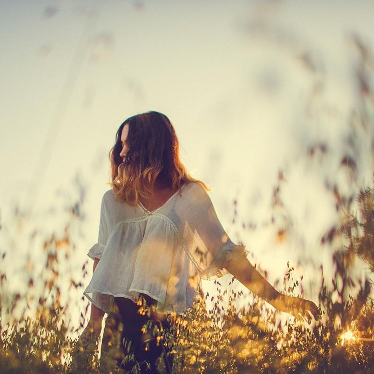 a woman standing in tall grass with her arms spread out to the side as the sun goes down