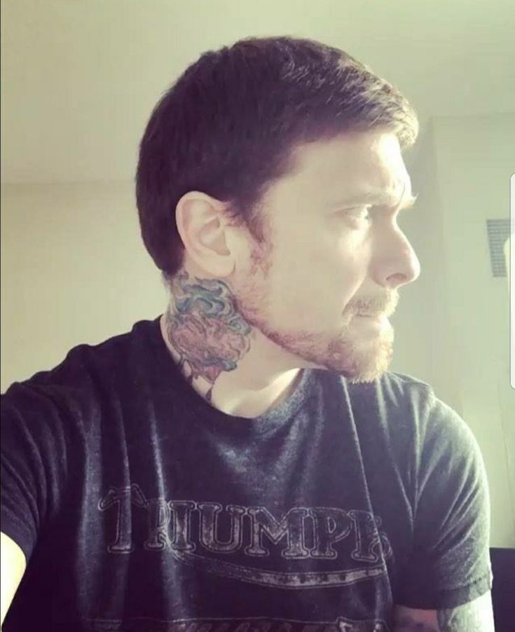 a man with tattoos on his neck and chest standing in front of a mirror looking off to the side