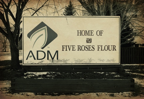 a sign for the home of five roses flour in front of some trees and bushes